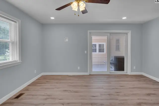 Spacious room with light blue walls, wood-look flooring, and a sliding glass door to the exterior.