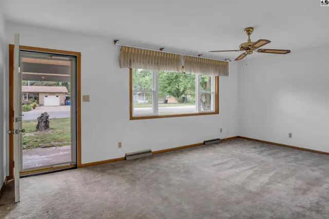 Spacious living room with carpet, large window, ceiling fan, and glass door to exterior.
