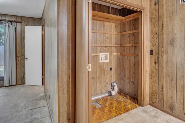 Wood-paneled room with an open closet featuring shelving, laundry hookups, and patterned flooring.