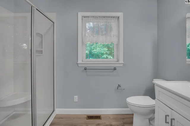 Modern bathroom with a white shower stall, light wood floors, and a white vanity.