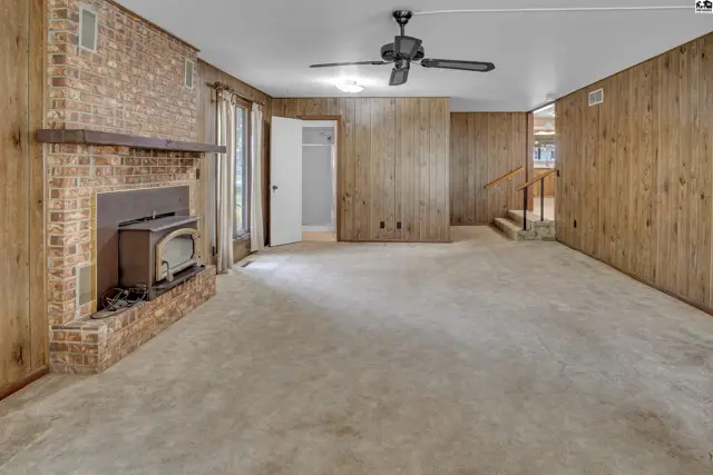 Spacious living room with brick fireplace, wood paneling, and plush carpet.