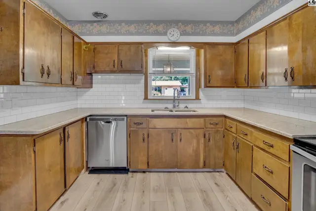 U-shaped kitchen with warm wood cabinets, white subway tile backsplash, and light wood laminate flooring.