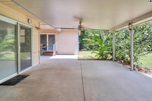 Covered patio with concrete floor, ceiling fan, and surrounding greenery.