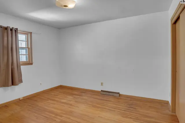 Empty bedroom with hardwood floors, a window with brown curtains, and a closet door.