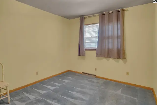 A simple bedroom with pale yellow walls, a patterned carpet, and brown curtains over a window.