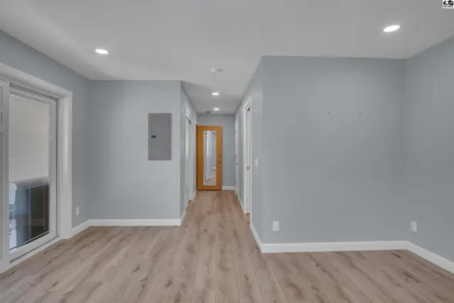 Hallway with light wood flooring, light blue walls, and a glass-paneled door at the end.