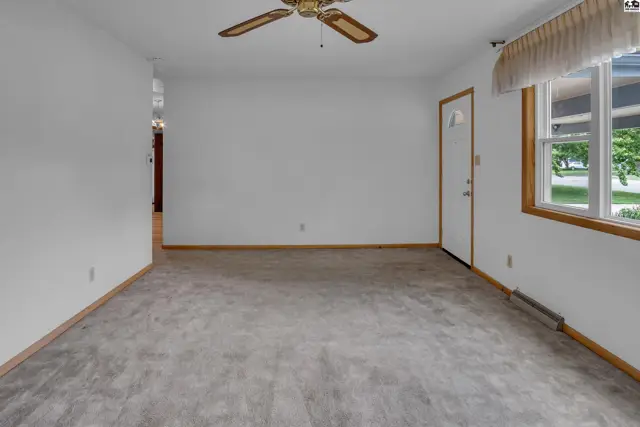 Spacious living room with neutral carpet, white walls, wood trim, and a ceiling fan.