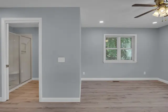 Spacious room with light gray walls, wood-look flooring, a ceiling fan, and an open doorway to a closet.