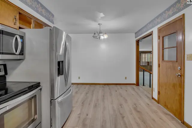 Stainless steel appliances and wood-look flooring in a dining area with a chandelier and patterned wallpaper.