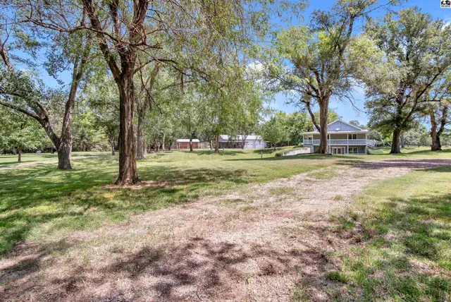 Spacious home with wraparound porch nestled among mature trees on a large, grassy lot.