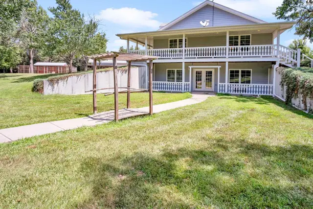 Spacious two-story home with a wraparound porch, white railings, and a wooden pergola in a grassy yard.