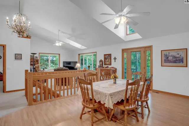 Spacious dining area with vaulted ceilings, skylights, wood railings, and a chandelier.