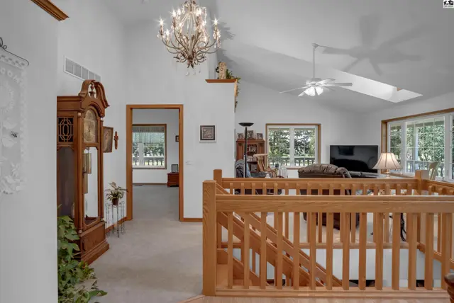Spacious living area with vaulted ceilings, a grand chandelier, and a wooden staircase overlooking the room.