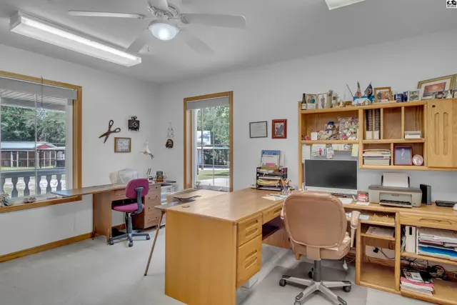 Spacious home office with two desks, built-in shelving, and natural light from large windows.