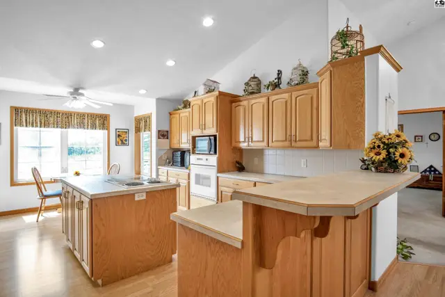 Spacious kitchen with light wood cabinets, white countertops, island, and breakfast bar.