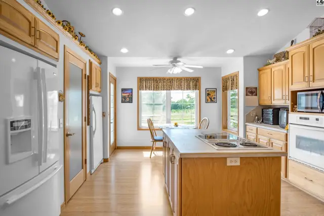 Spacious kitchen with light wood cabinets, stainless steel appliances, and a large island with a stovetop.