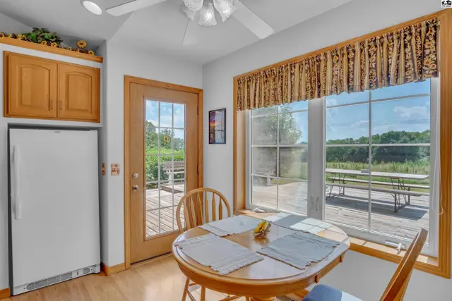 Bright kitchen nook with a round table, wooden cabinets, and large windows overlooking a deck and rural landscape.