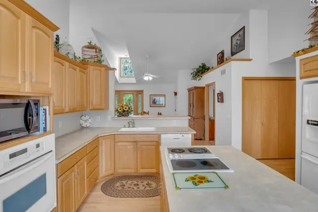 Spacious kitchen with light wood cabinets, granite countertops, and a large island with a stovetop.