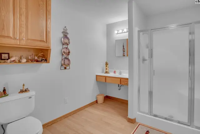 Bright bathroom with light wood vanity, laminate flooring, and a glass-enclosed shower.