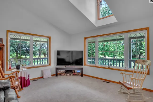 Spacious living room with vaulted ceiling, large windows, and light wood rocking chairs.