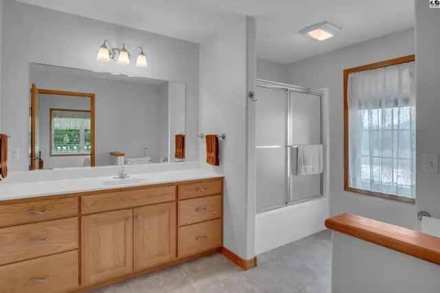 Spacious bathroom with a long oak vanity, large mirror, and a glass-enclosed shower.