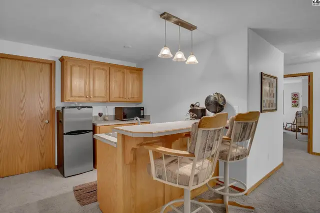 Kitchenette with light wood cabinets, stainless steel appliances, and a breakfast bar with rustic stools.