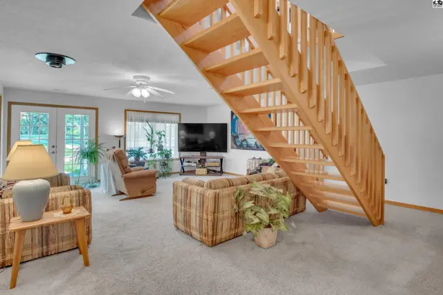 Living room with light carpet, wood staircase, and comfortable seating.