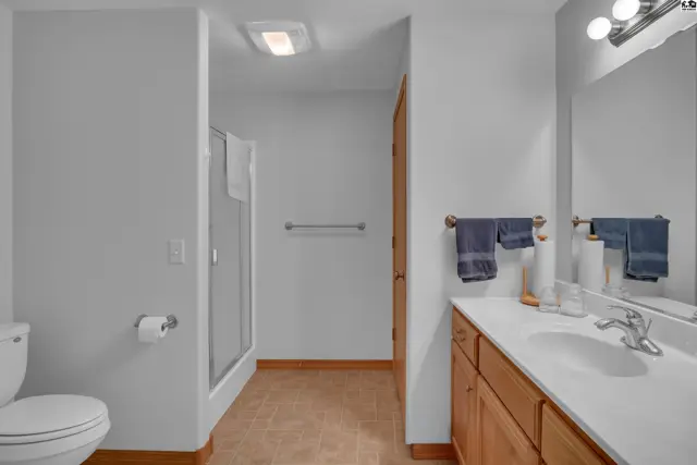 Modern bathroom with a glass-enclosed shower, light wood vanity, and beige tile flooring.