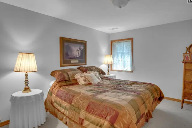 Cozy bedroom with a queen-size bed, patterned bedding, and a wooden dresser.
