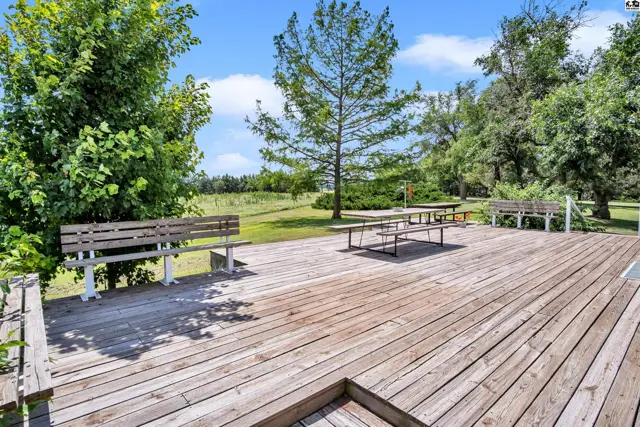 Spacious wooden deck with picnic tables and benches surrounded by lush green trees.