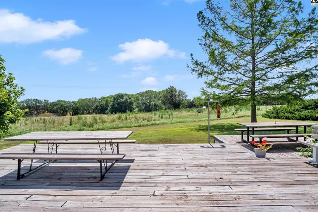 Wooden deck with picnic tables overlooks a scenic green landscape under a bright blue sky.