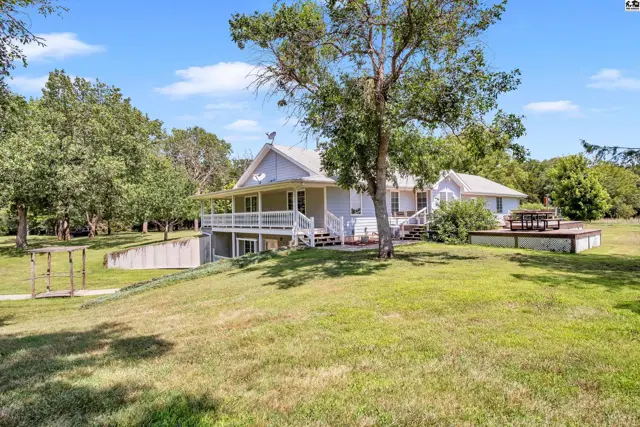 Spacious light-colored home with a wraparound porch, deck, and mature trees on a grassy lot.