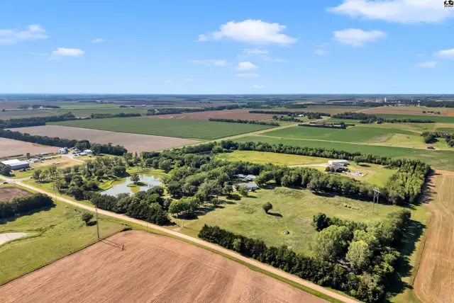 Expansive aerial view of a rural property with a pond, mature trees, and surrounding agricultural fields.