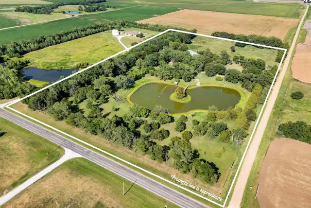 Aerial view of a sprawling property featuring a large pond, mature trees, and a distant house.