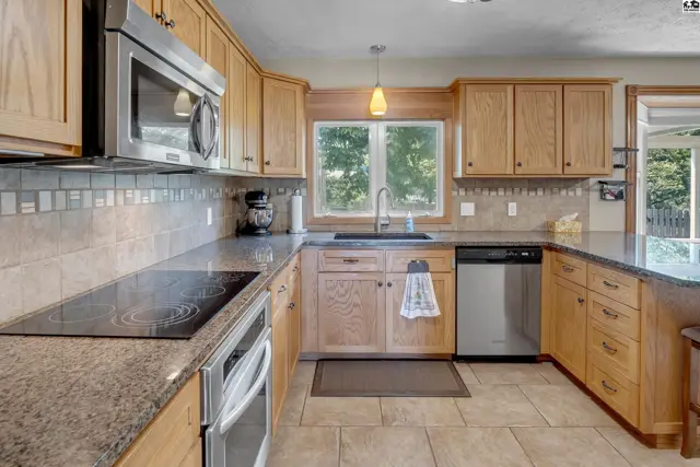 Spacious kitchen with light wood cabinets, granite countertops, stainless steel appliances, and tile backsplash.