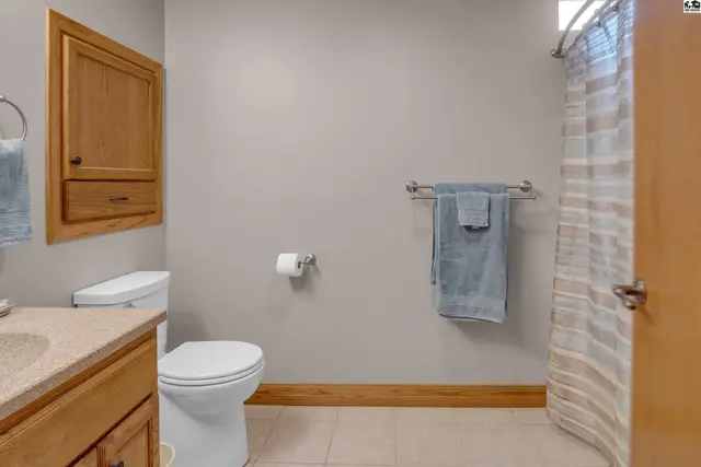 Neutral bathroom with wood cabinetry, tiled floor, and a striped shower curtain.