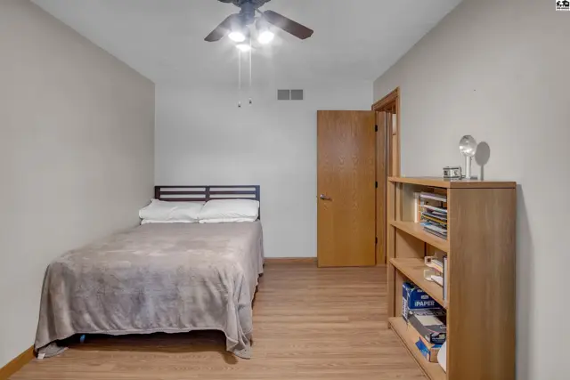 Bedroom with a bed, wooden floors, ceiling fan, and a bookshelf.