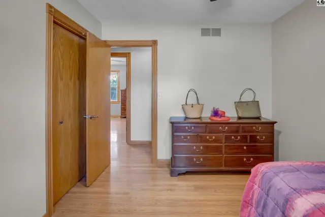 Bedroom with light wood floors, a dark wood dresser, and two doors.
