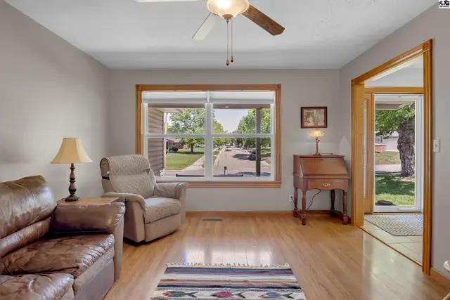 Living room with leather sofa, recliner, wood floors, and large window overlooking a tree-lined street.