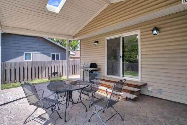 Covered patio with stamped concrete, outdoor dining set, and grill next to a sliding glass door.