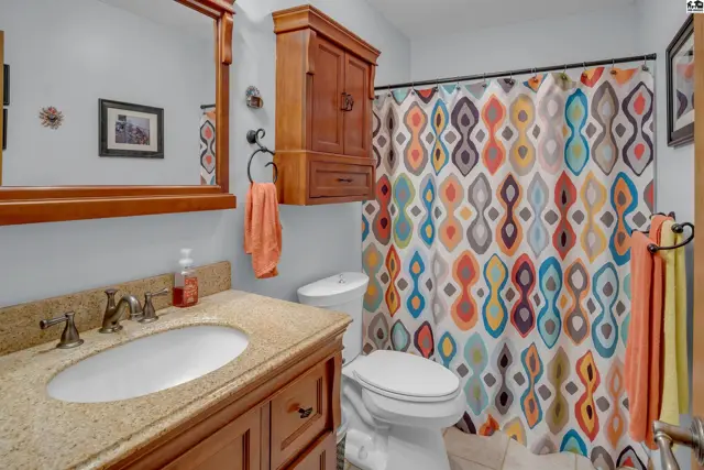 Bright bathroom with granite vanity, wood cabinetry, and a colorful, patterned shower curtain.