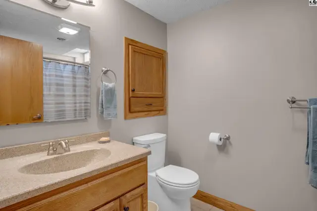 A neutral bathroom features a vanity with a speckled countertop, wood cabinetry, and a toilet.