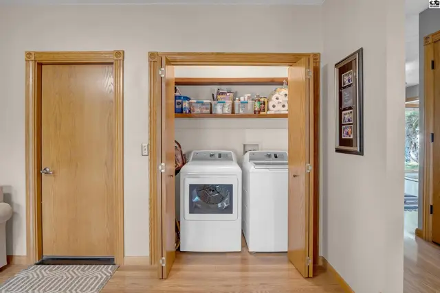 Laundry room with white washer and dryer, wood floors, and a shelved storage area.
