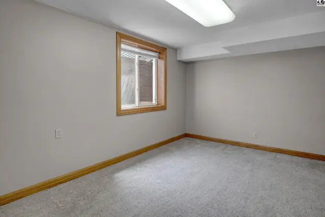 Empty room with light gray carpet, neutral walls, and a wooden-trimmed window.