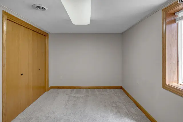 Empty room with light gray walls, beige carpet, and a large wooden closet.