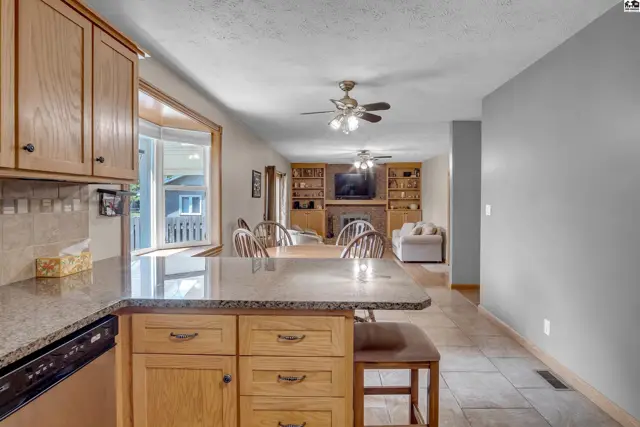 Kitchen island with granite countertop and wood cabinets opens to a living room with built-in shelves.