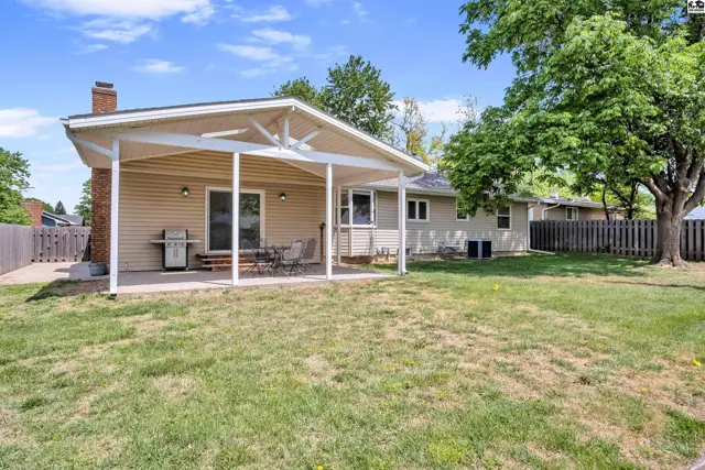 Covered patio with seating overlooks a grassy backyard with a tan vinyl-sided home.