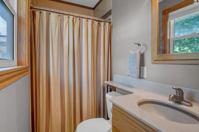 Bright bathroom with a beige and white striped shower curtain, light wood vanity, and a marble countertop.