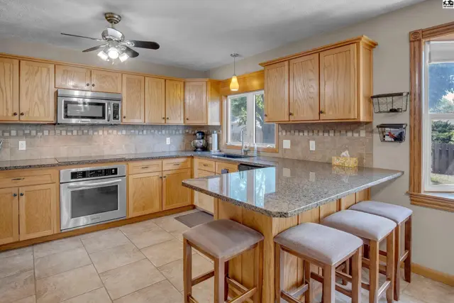 Spacious kitchen with light oak cabinets, granite countertops, stainless steel appliances, and a breakfast bar.
