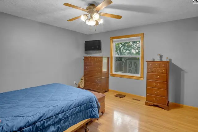 Spacious bedroom with gray walls, hardwood floors, a blue bed, and wooden dressers.